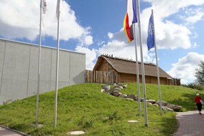 Ein grasbewachsener Hügel mit einer traditionellen Holzbauten, einem gepflasterten Weg und Flaggen.