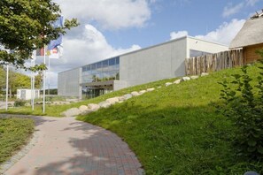 A modern building with a glass facade, a paved pathway, and a grassy area with rocks. - Holiday home in Damp with swimming pool (Damp)