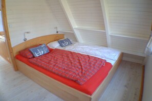 A single bed with a red blanket and pillows, a wooden headboard, and a sloped ceiling. - Holiday home in Damp with swimming pool (Damp)