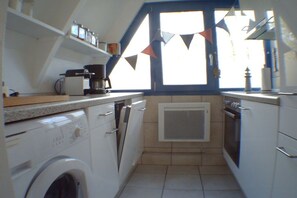 Eine kleine Küche mit Waschmaschine, Backofen und einem Fenster mit dreiecklicher Verzierung.