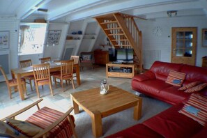 A cozy living room with a wooden table, red leather sofa, and a wooden staircase. - Holiday home in Damp with swimming pool (Damp)