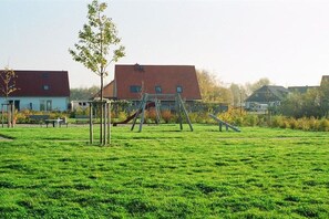 A playground with swings and slides in a grassy area with houses in the background. - Holiday home with 1 bedroom (Kaltenhof (Insel Poel))