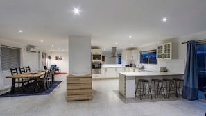 Une cuisine moderne dotée d’un îlot central, de tabourets de bar et d’un coin repas avec une table et des chaises en bois.