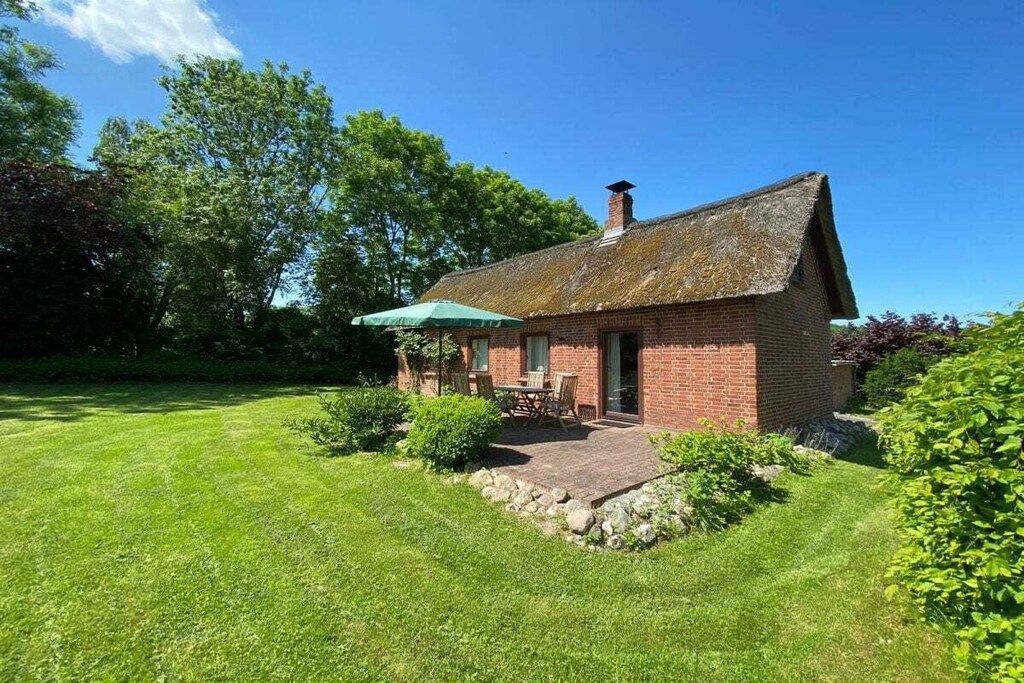 A brick house with a thatched roof, a small patio with a table and chairs, and a green umbrella.