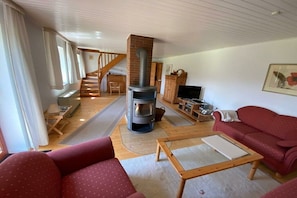 A cozy living room with a fireplace, red sofas, wooden flooring, and a staircase leading to another level. - Holiday home in Waabs with swimming pool (Waabs)