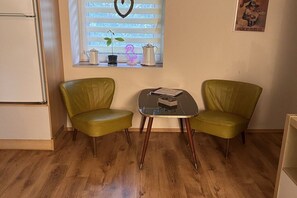 A small room with two green chairs and a small table, a window with blinds, a refrigerator, and a poster on the wall. - Holiday home in Tann with swimming pool (Tann)