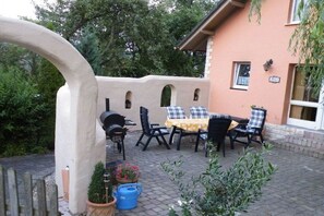 An outdoor patio with a table and chairs, a barbecue grill, and potted plants. - Holiday home in Tann with swimming pool (Tann)