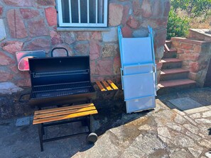Edifici de pedra amb una barbacoa i una cadira plegable blava.
