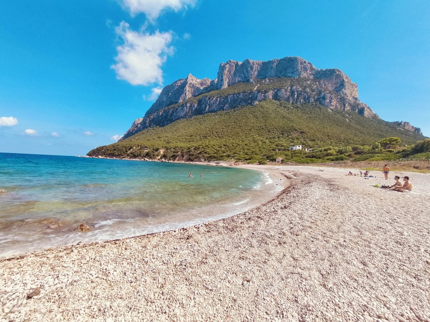 A pebble beach with clear water and a large mountain in the background.