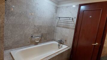 A bathroom with a bathtub, a towel rack, and a wooden door.