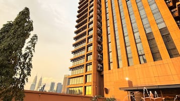 Un edificio moderno de gran altura con un diseño vertical llamativo, rodeado de jardines ajardinados y un elemento acuático.