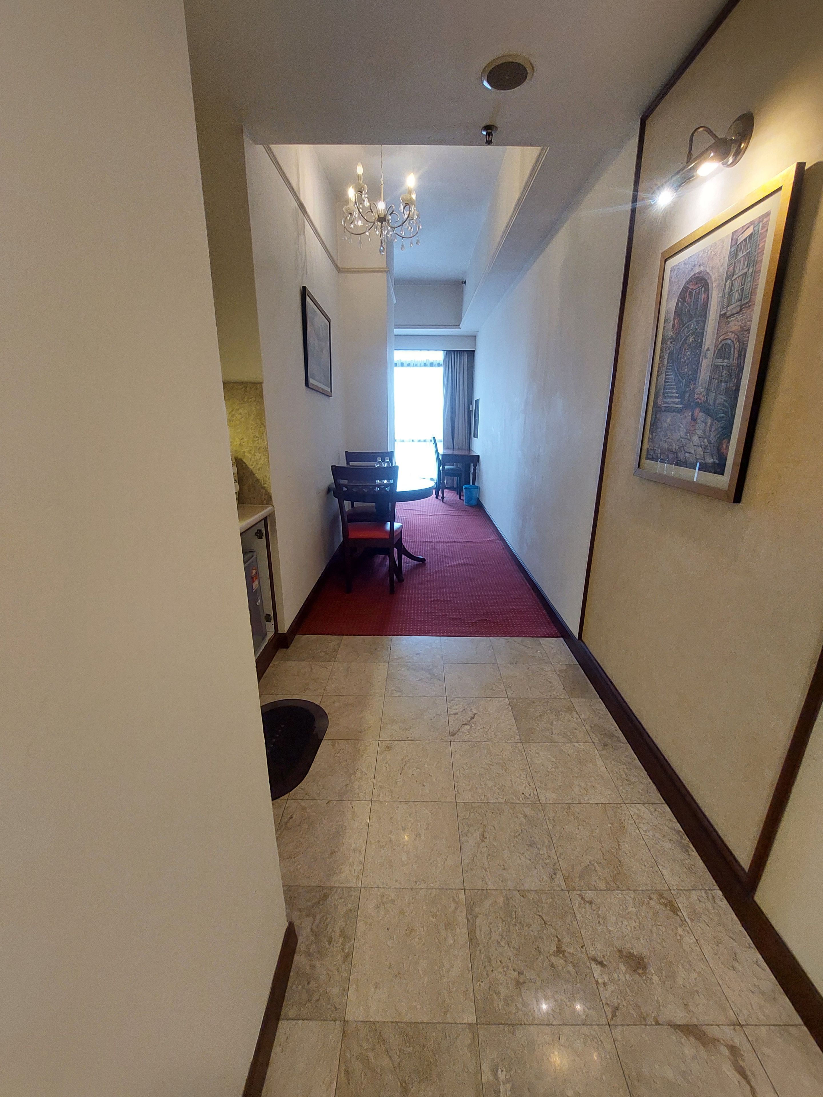 Ein Hotelkorridor mit Essbereich, einer Kristallleuchtre und einem gerahmten Kunstwerk an der Wand.
