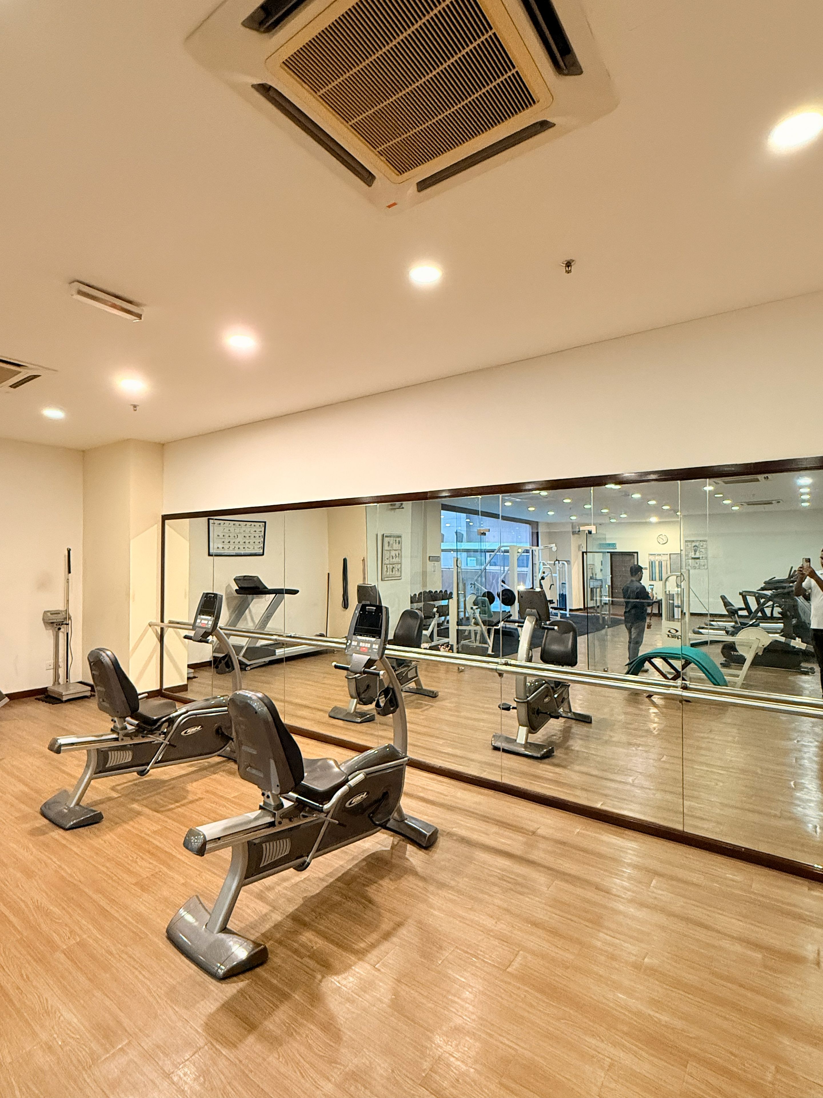A gym with exercise equipment, a large mirror, and a wooden floor.