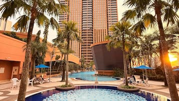 A hotel with a large pool, palm trees, and a modern building in the background.