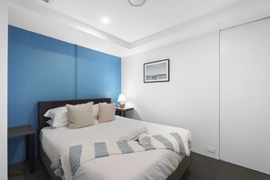 A hotel room with a bed, a nightstand, a lamp, and a framed picture on the wall. - Ocean View Circle on Cavill 2BR Apartment (Gold Coast)