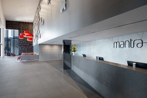 A modern reception area with a marble wall, a reception desk, and a seating area with a red pendant light. - Ocean View Circle on Cavill 2BR Apartment (Gold Coast)