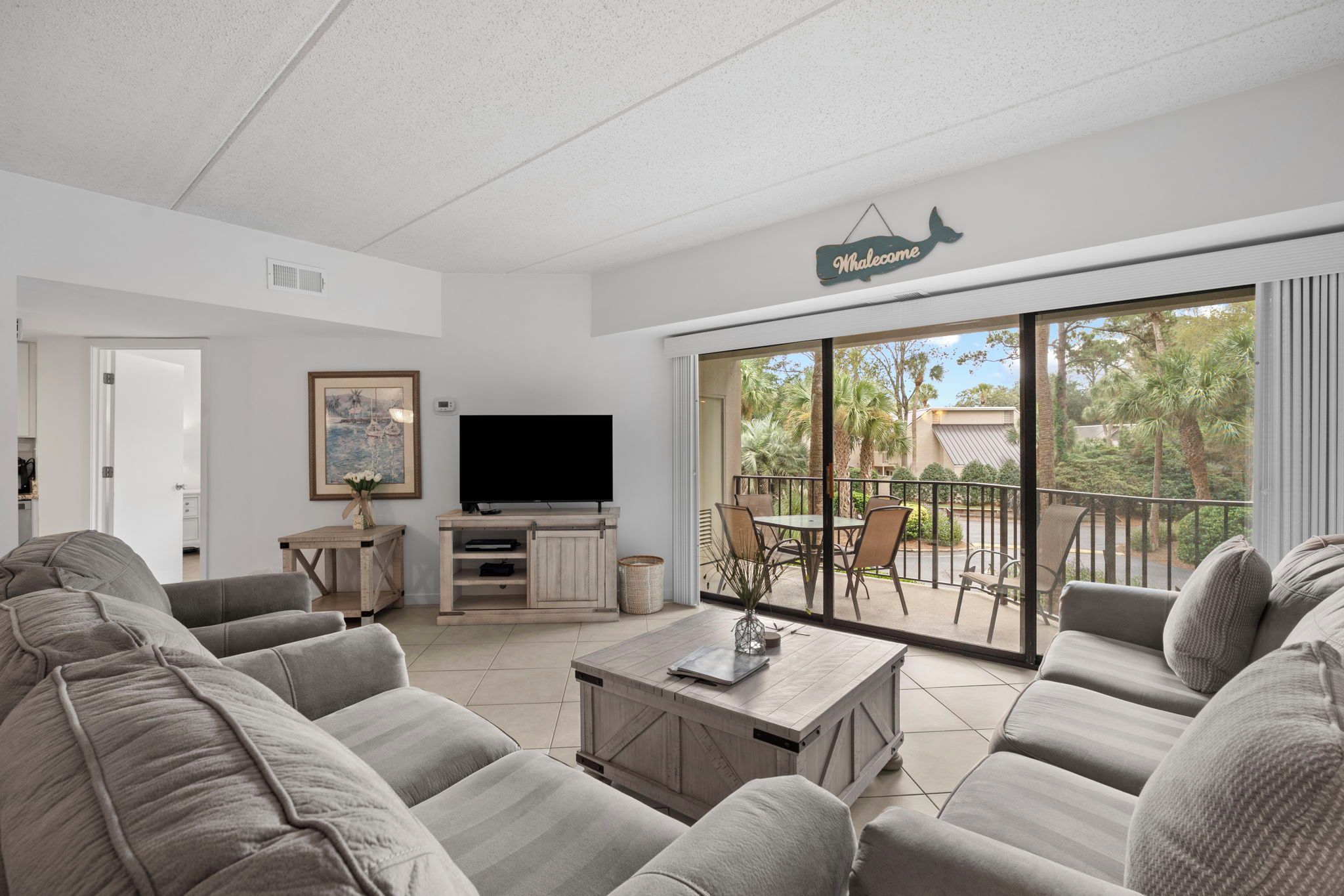A living room with a television, sofa, coffee table, and a balcony with outdoor seating.