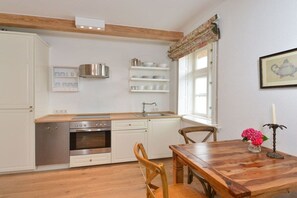 A kitchen with white cabinetry, a wooden countertop, a stove, and a dining table with chairs. - Paulsen Cottage||Gelting (Gelting)