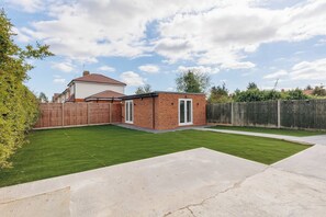 Een achtertuin van een woning met een verzorgd gazon, een bakstenen gebouw en een houten omheining.