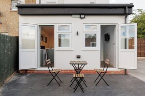 Ein Haus mit einer Terrassenfläche, komplett mit Tisch und Stühlen, einer sichtbaren Küche und einer Tür zu einem Innenraum.