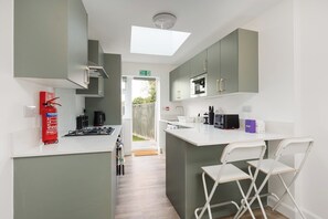 A modern kitchen with a central island, white bar stools, and a fire extinguisher. - Lovely 4BR Hayes Home | Parking | Near Heathrow (Greater London)