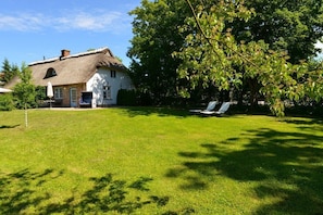 A house with a thatched roof, a lawn, and two lounge chairs. - Holiday apartment with 1 bedroom (Gelting)