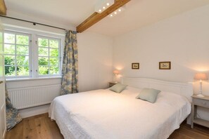 A bedroom with a large bed, two bedside lamps, a window with curtains, and a radiator. - Holiday apartment with 1 bedroom (Gelting)