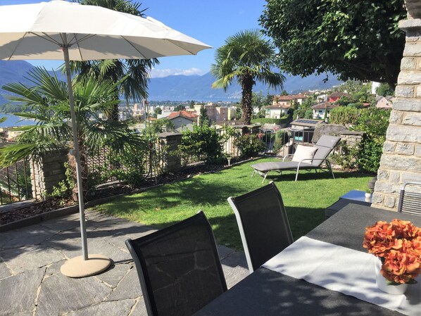 Een terras buiten met een tafel, stoelen en een parasol.