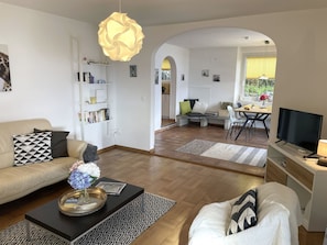 A modern living room with a sofa, coffee table, and a TV. There is a bookshelf and a dining area with a table and chairs. - La Margarita by Interhome (Minusio)