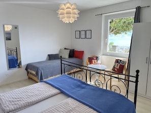 A bedroom with two beds, a window with a view, a small table, and a hanging light fixture. - La Margarita by Interhome (Minusio)