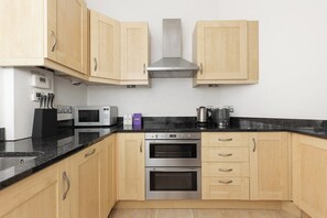 A modern kitchen with light wood cabinets, a black countertop, stainless steel appliances including a microwave, toaster, and oven, and a stainless steel range hood. - New! Delightful 2BR w/Balcony | Chelsea (Greater London)