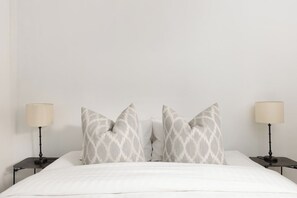 Un lit avec une literie blanche, deux tables de chevet avec des lampes et des coussins à motifs.