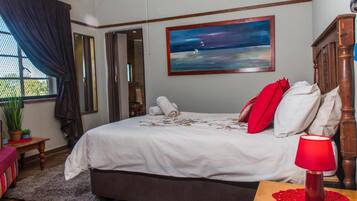 A bedroom with a bed, a nightstand, a red lamp, a painting, and a window with curtains.