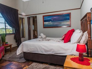 A bedroom with a bed, a nightstand, a red lamp, a painting, and a window with curtains. - Toeka Wedding & Function Venue (Lethabong)
