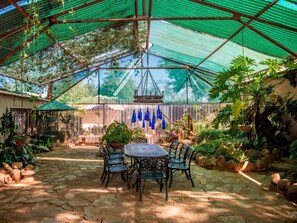 A covered patio with a table and chairs, surrounded by potted plants and a variety of greenery. - Toeka Wedding & Function Venue (Lethabong)