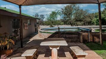 An outdoor patio area with a table and benches, a swimming pool, and a building with a gate.