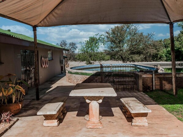 An outdoor patio area with a table and benches, a swimming pool, and a building with a gate. - Toeka Wedding & Function Venue (Lethabong)
