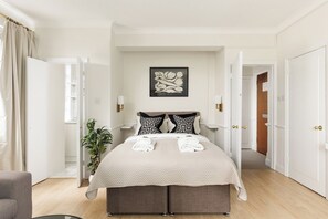 Een netjes ingerichte slaapkamer met een bed, nachtlampjes, een kunstwerk aan de muur en een potplant.