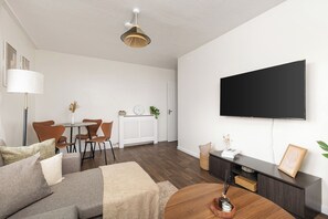 A modern living room with a sofa, coffee table, and a flat-screen TV mounted on the wall. - New! Light-Filled & Cosy 2BR Flat | Woolwich (Greater London)