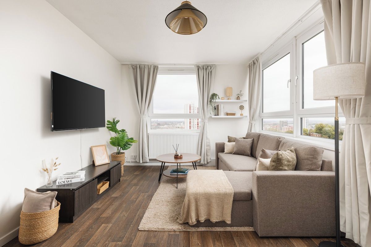 A modern living room with a flat-screen TV, a sofa, a coffee table, and a large window with curtains.