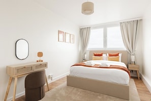 A bedroom with a bed, bedside table, lamp, and a desk with a chair. - New! Light-Filled & Cosy 2BR Flat | Woolwich (Greater London)