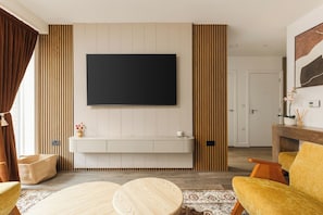 A modern living room with a flat-screen TV mounted on the wall, a wooden bench below, and a yellow sofa. - New! Stylish 1BR w/Balcony by Olympic Park (Greater London)