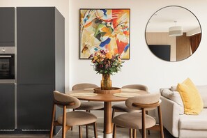 A modern dining area with a round table, six chairs, a vase of flowers, and a colorful abstract painting on the wall. - New! Stylish 1BR w/Balcony by Olympic Park (Greater London)