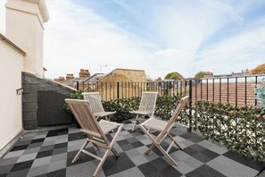 A rooftop terrace with two wooden chairs, a checkered floor, and a view of buildings in the background. - Peaceful 2BR Fulham Maisonette | Private Terrace (Greater London)