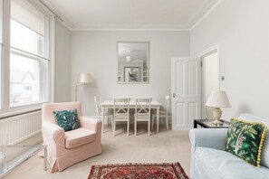 A room with a dining table, chairs, a sofa, a chair with a cushion, a lamp, and a rug. - Peaceful 2BR Fulham Maisonette | Private Terrace (Greater London)