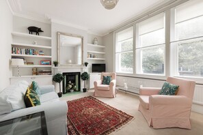 Een woonkamer met een open haard, boekenkasten, een televisie en twee fauteuils.