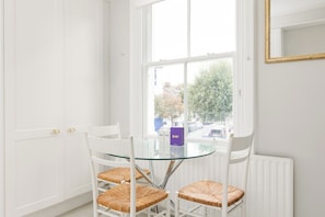 A room with a glass table and four wicker chairs, a white radiator, and a window with a view of the outside. - Peaceful 2BR Fulham Maisonette | Private Terrace (Greater London)