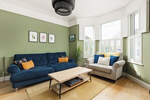 Ein Wohnzimmer mit einem blauen Sofa, einem gestreiften Sofa, einem Holztisch und einer grünen Wand mit gerahmten Bildern.