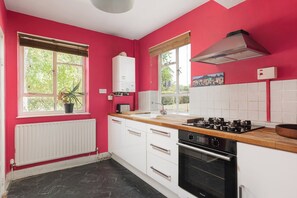 A kitchen with white cabinets, a black oven, a gas stove, and a window with a plant. - New! Characterful 3BR Flat | Peckham Rye Park (Greater London)