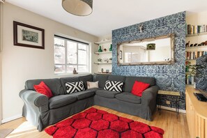 A living room with a grey sectional sofa, red and black patterned rug, and a blue patterned wall. - New! Characterful 3BR Flat | Peckham Rye Park (Greater London)
